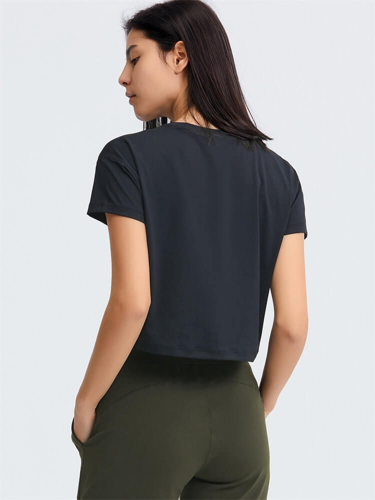 Woman wearing a black loose fit workout crop t-shirt, perfect for yoga, highlighting short sleeves and breathable fabric.